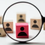 Lupa powiększająca różowy klocek symbolizujący pracownika B2B lub na zlecenie w kontekście analizy zmian w Kodeksie pracy od 1 maja, wśród innych klocków na białym tle.