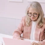 Kobieta na emeryturze pracująca na laptopie w jasnym biurze, co ilustruje temat łączenia własnej firmy z wcześniejszą emeryturą i limitami ZUS.