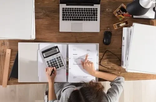 High Angle View Of A Businesswoman Calculating Invoice On Office Desk